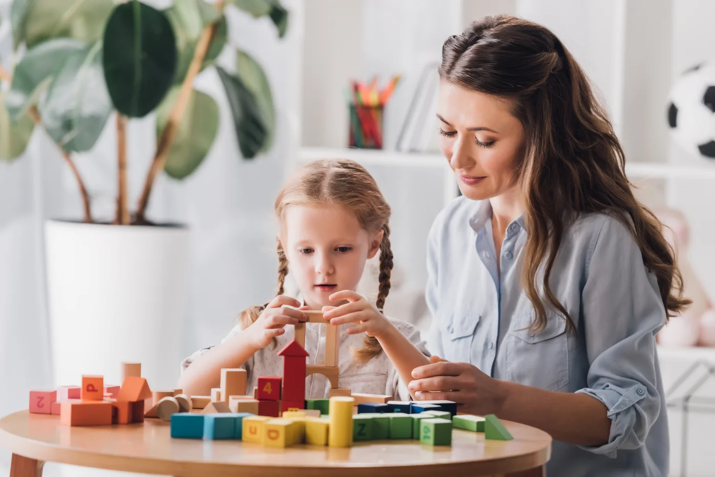 Terapeuta e menina montando blocos de madeira sobre uma mesa